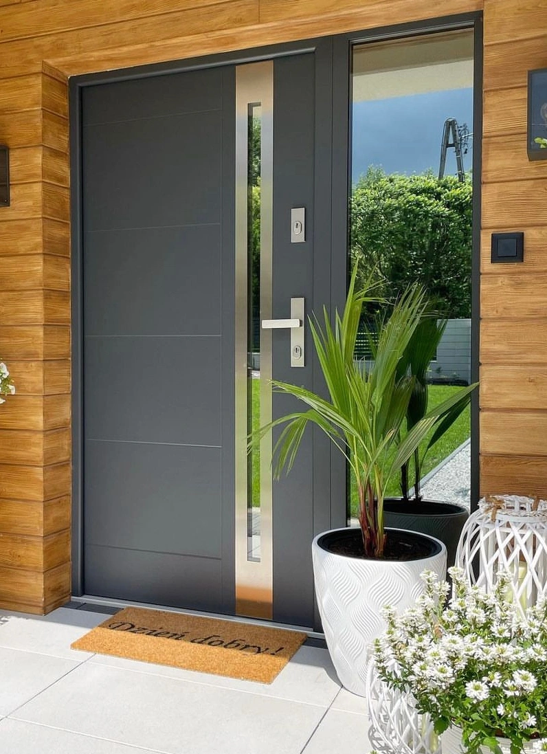 Modern dark grey cast aluminum exterior system door with a vertical glass insert and metal handle for luxury villas.